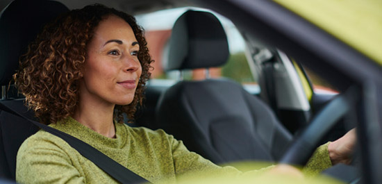 A contented driver, smiling and relaxed, sits behind the wheel of a car, enjoying a pleasant drive on a sunny day.